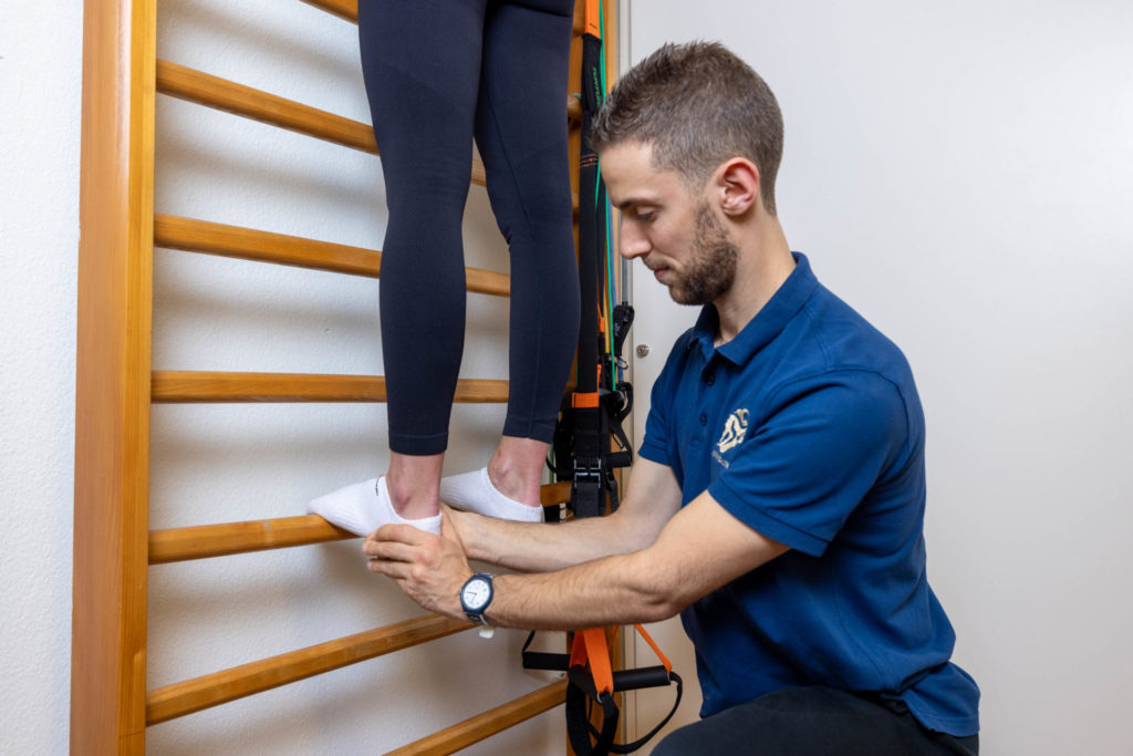 Physiotherapeut behandelt den Fuss einer Patientin an der Sprossenwand in Basel